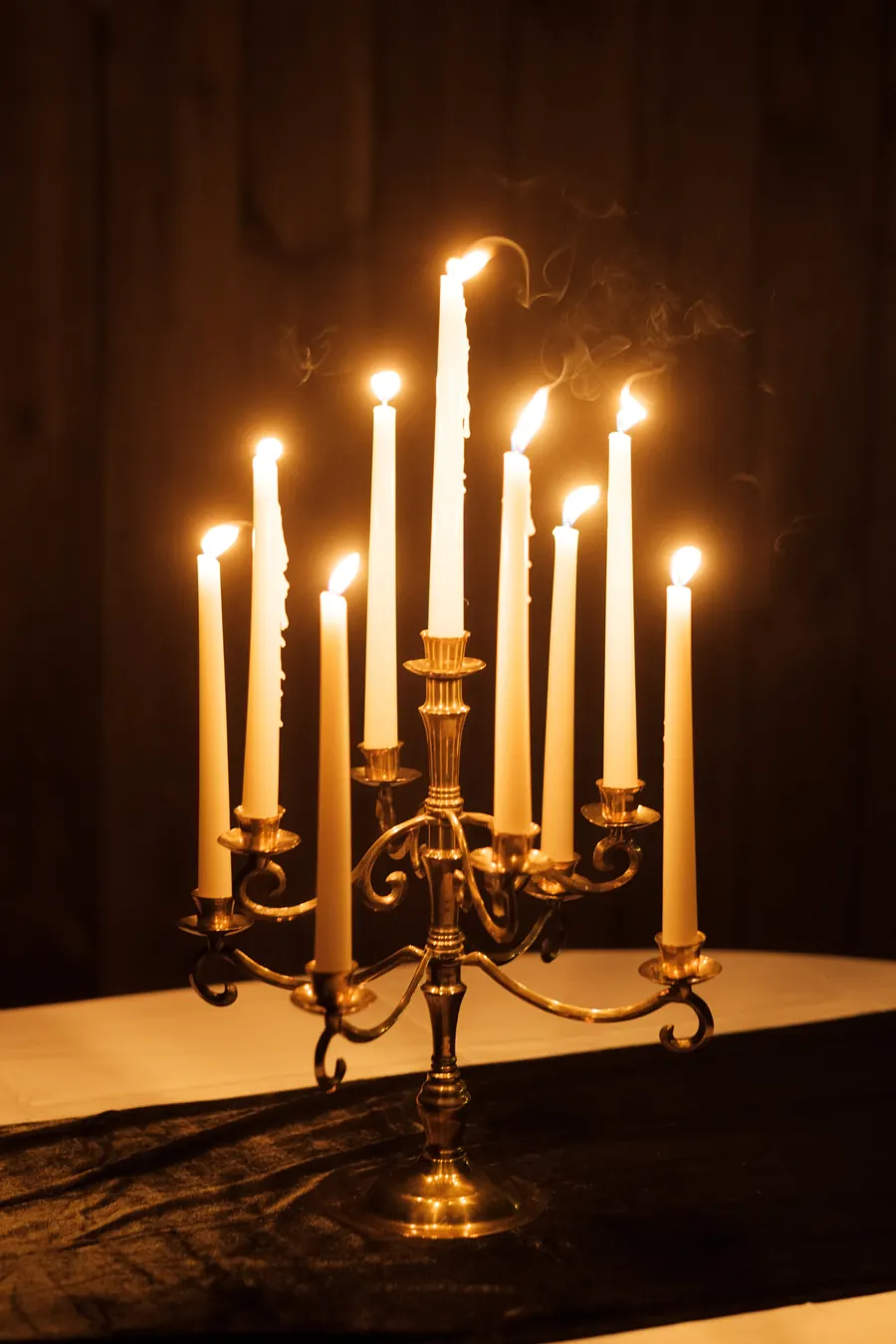 The 9 arm brass candelabra with all nine white tapers lit, on a dark table runner