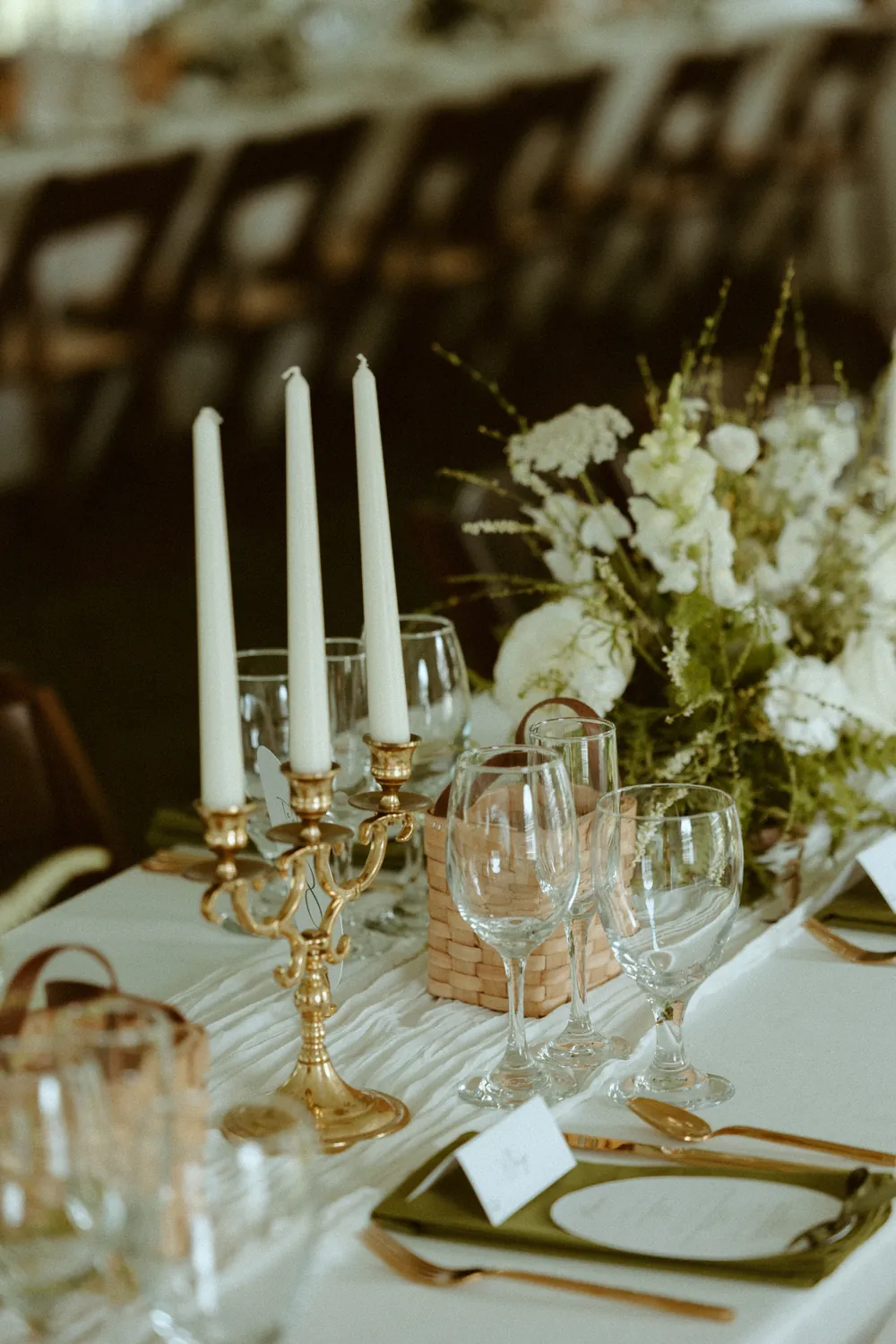 A reception table set with brass candelabras, taper candles and white florals