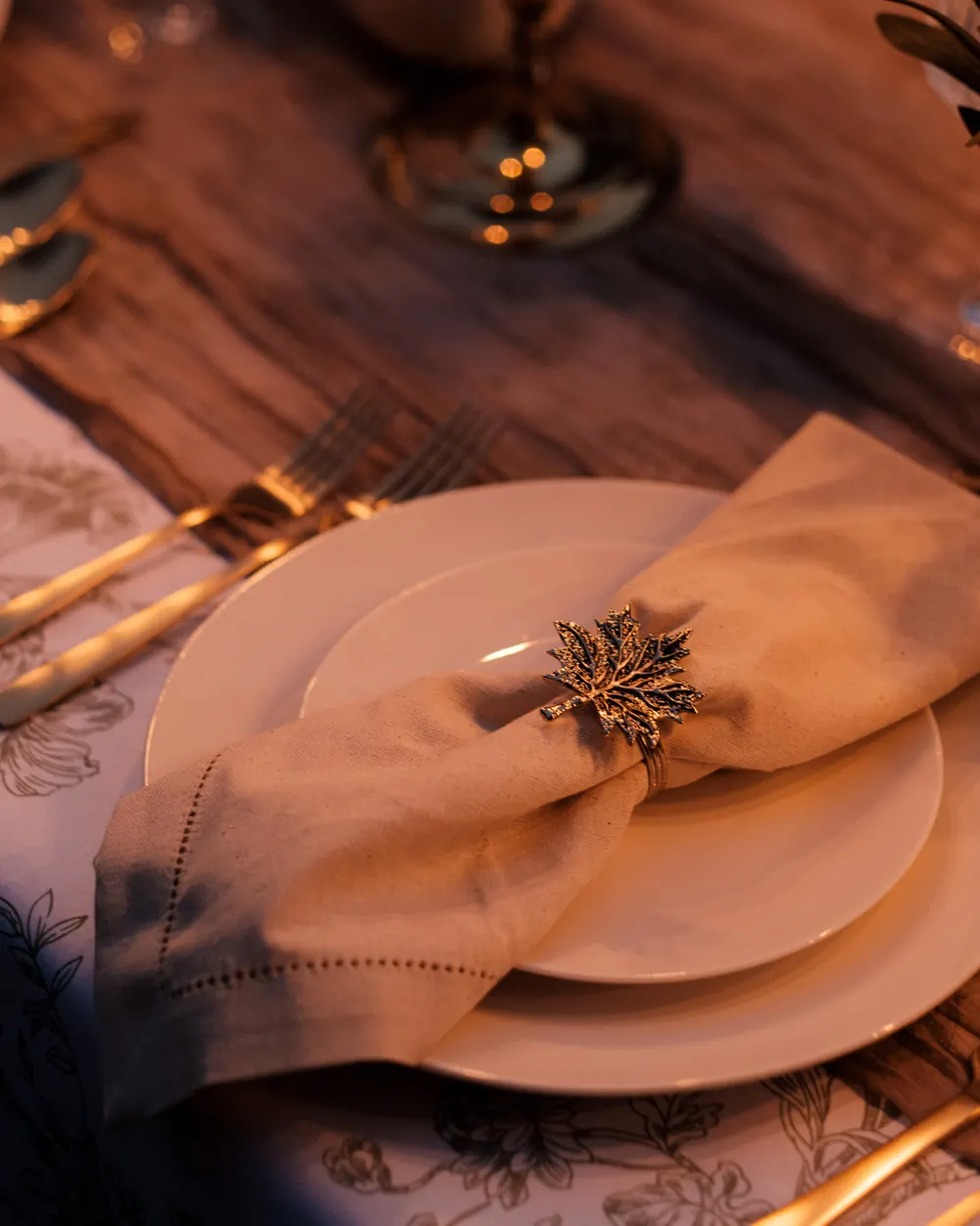 A white round salad plate stacked on a dinner plate, with a cream napkin and gold leaf napkin ring on toile linen