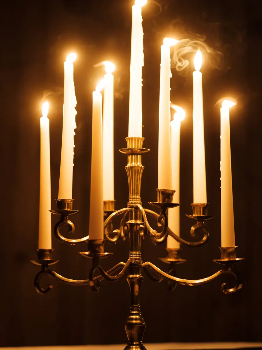 A brass candelabra glowing with a cluster of lit white taper candles