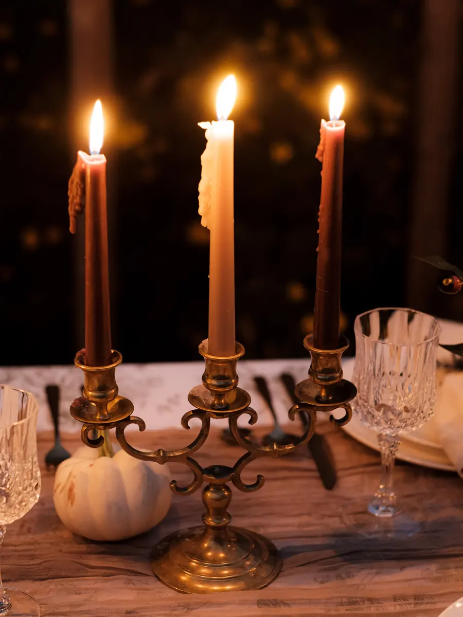 A three arm brass candelabra with lit tapers, a crystal goblet and a white pumpkin
