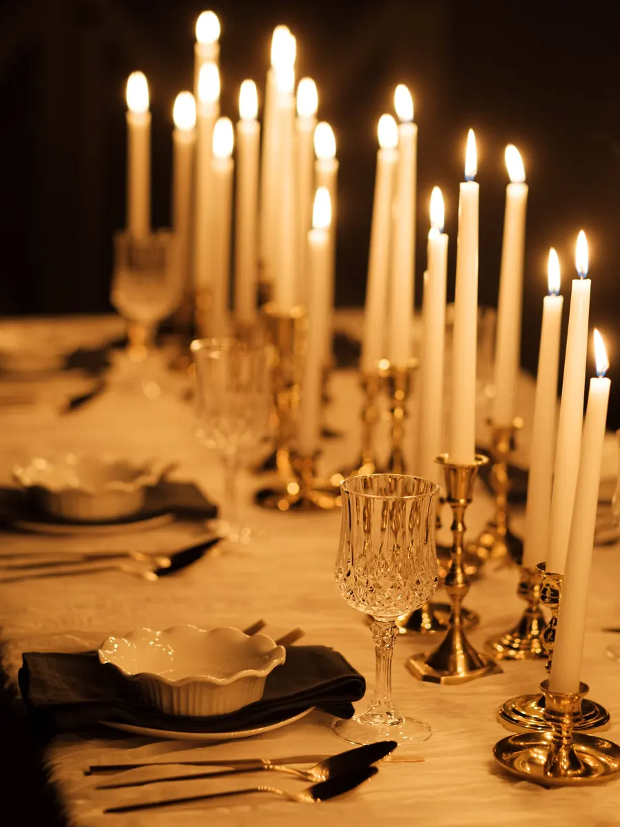 A candlelit table of tall tapers in brass holders with crystal goblets and a scalloped bowl